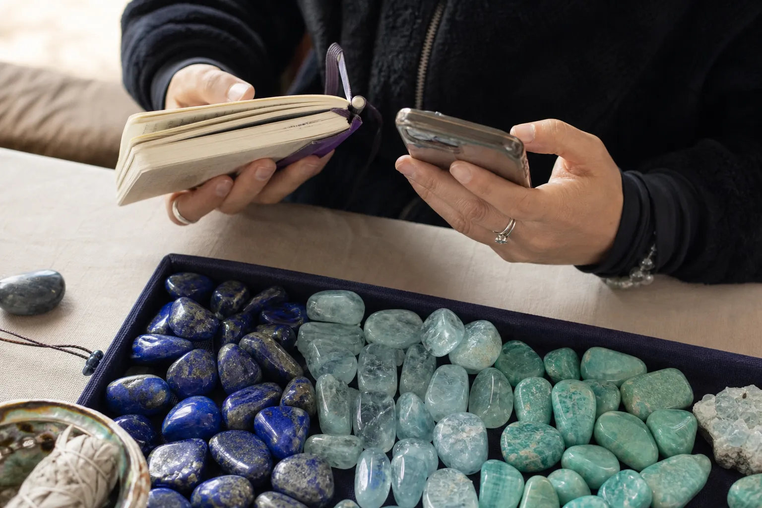 A reader comparing crystal notes beside lapis lazuli, aquamarine, and amazonite stones